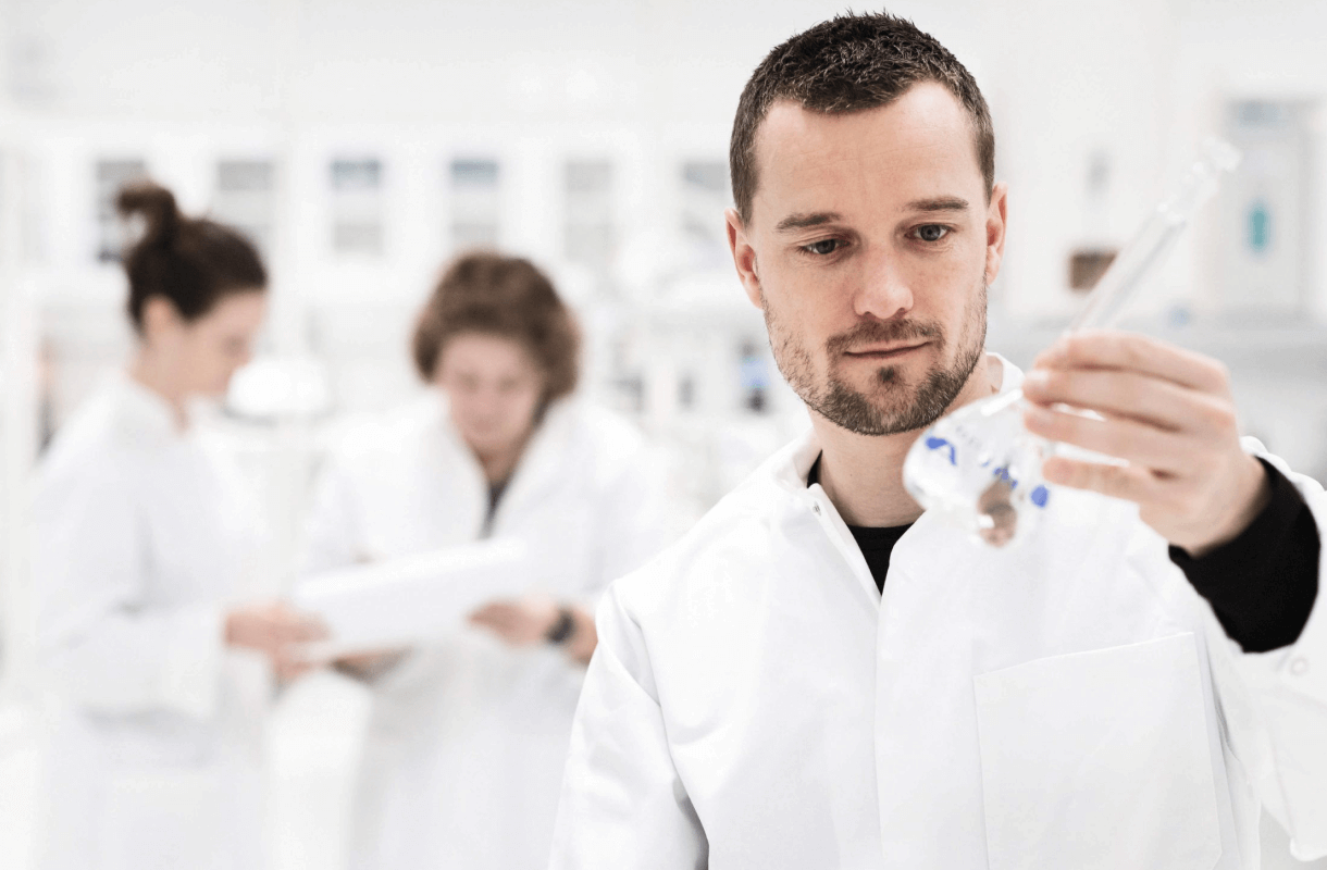 A person in a lab coat holding a beaker of water